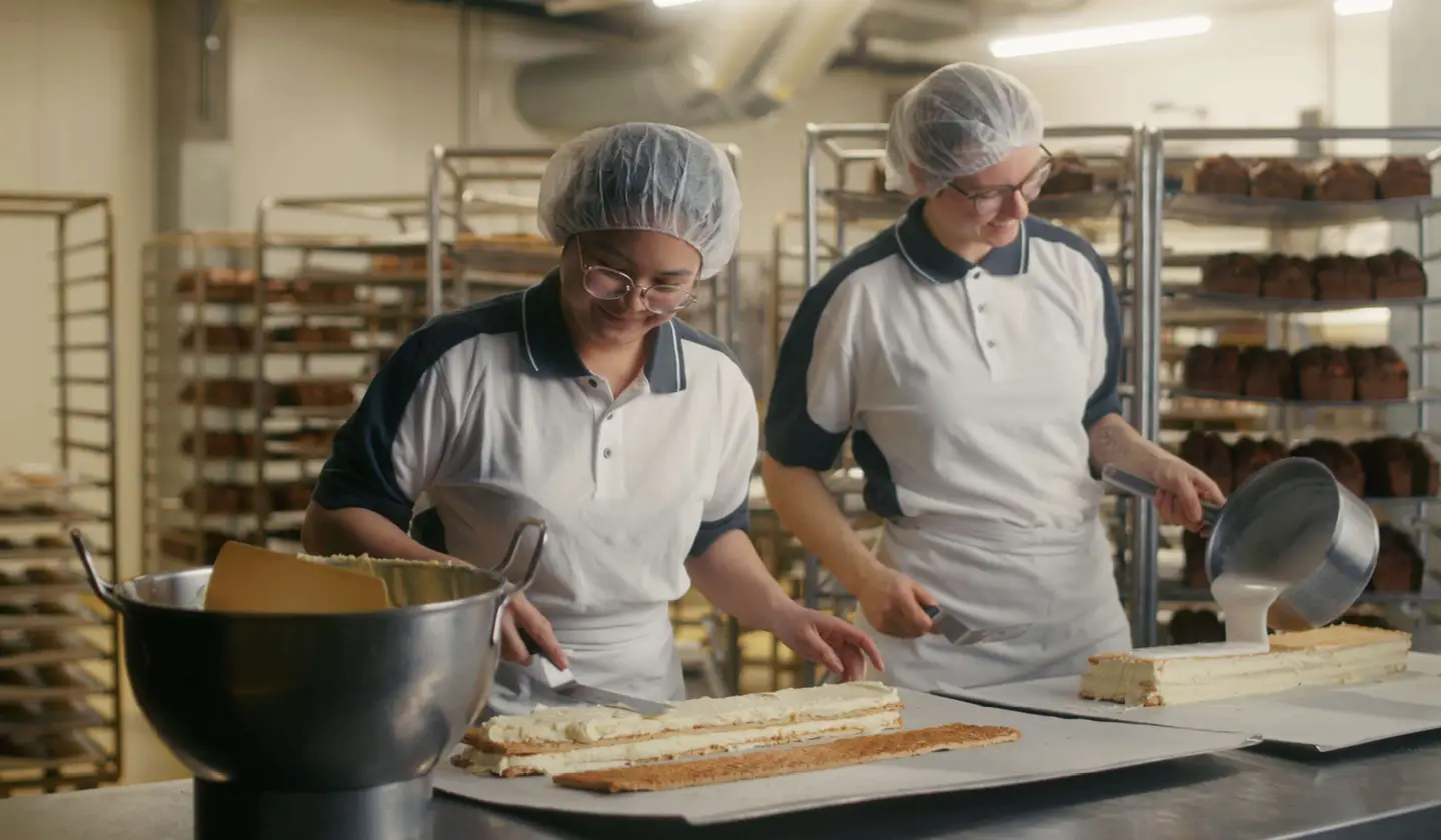 Zwei Bäckerinnen bestreichen und glasieren Kuchen in der Backstube.