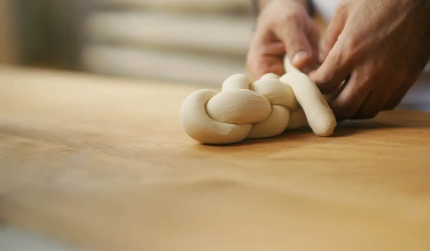 Hände flechten einen Teig zu Zopf.
